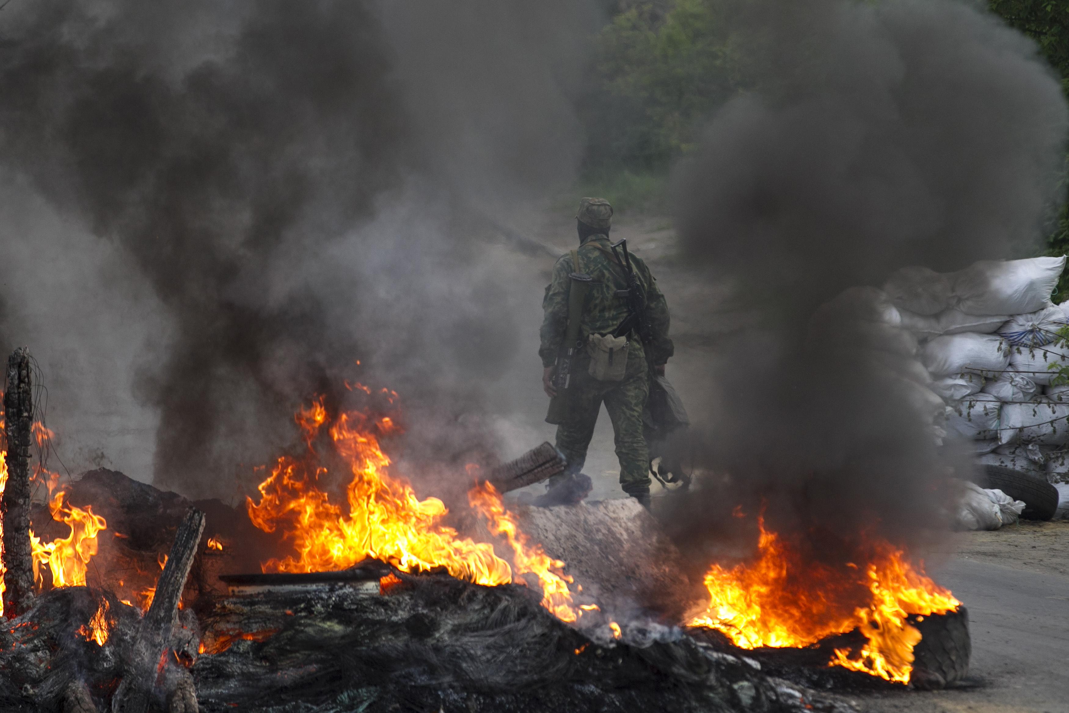 A pro-Russian separatist guards a checkpoint while walking near burning tyres near the town of Slaviansk